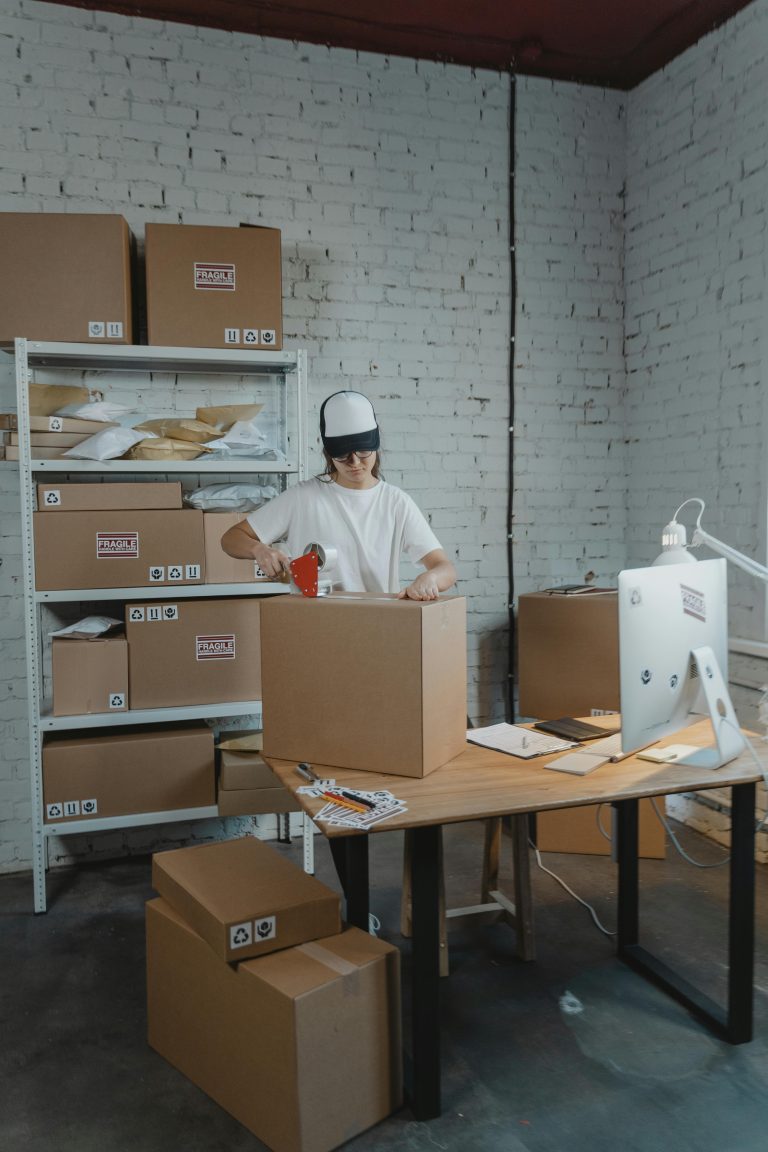 A warehouse worker in uniform packaging boxes for delivery in an organized storage area.